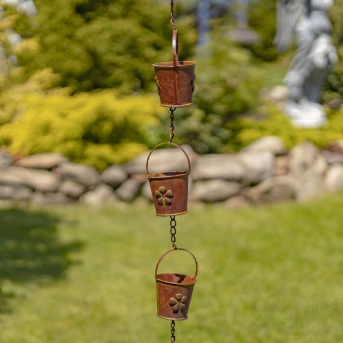 Decorative metal rain chain with floral designs in a garden setting