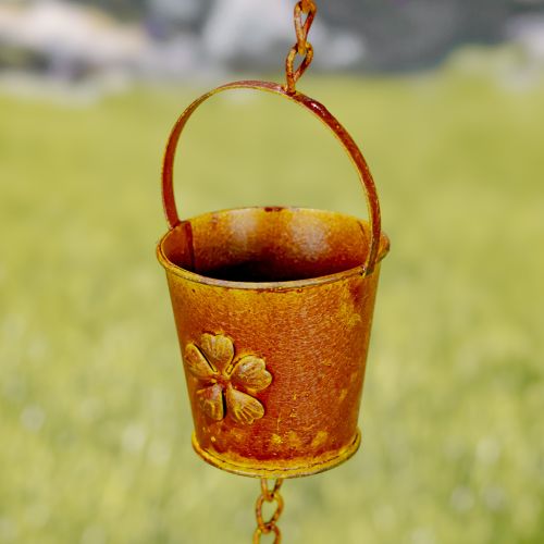Rust-colored metal bucket with a handle and clover design on a blurred green background