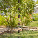 Decorative metal wind chime hanging in a garden with trees and grass in the background