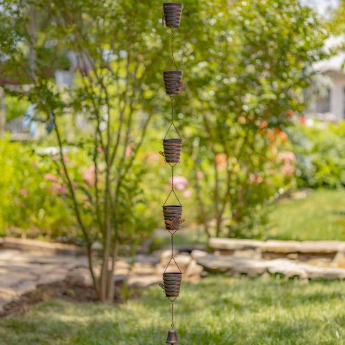 Decorative metal wind chime hanging in a garden with trees and grass in the background
