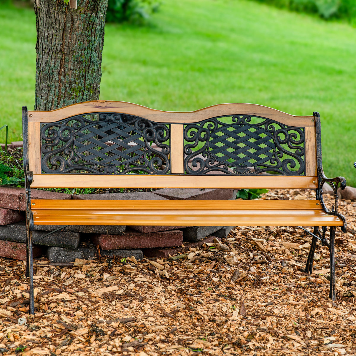 Wooden and iron bench sitting on mulch in front of a tree and a grassy meadow